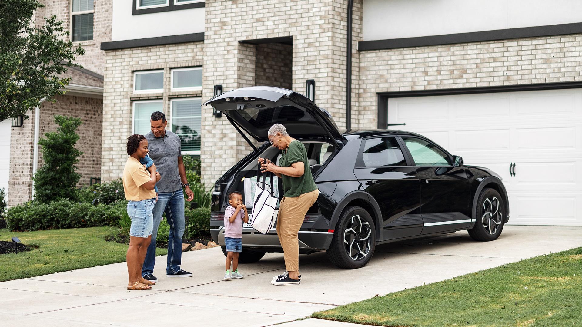 Dans une entrée d’auto résidentielle, une grand-maman sort un sac du coffre de son VUS au grand plaisir de son petit fils et des parents non loin tenant leur bébé. Tous semblent paisibles.